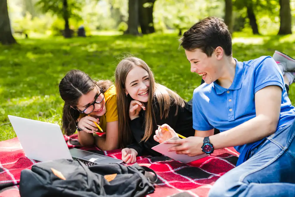 Jóvenes felices disfrutando de un pícnic y estudiando en un día soleado.